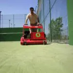 SMG TurfSoft TS2 artificial turf cleaner being pushed across a green turf field, cleaning the surface efficiently.