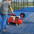 SMG TurfSoft TS3 artificial turf cleaner being operated on blue turf, effectively sweeping debris with its large rotating brush.