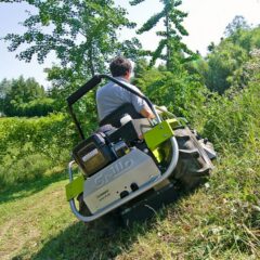 Rear view of a Grillo ride-on mower navigating through tall grass and vegetation