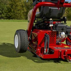 A red ride-on greens roller with a hydraulic drive, shown from the rear on a golf course