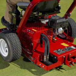 Close-up of a red ride-on greens roller with hydraulic components on a golf course green