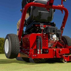 A red ride-on greens roller with a hydraulic drive, shown from the rear on a golf course