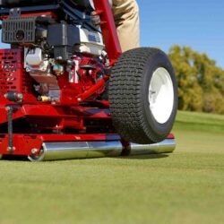 Close-up of a red ride-on greens roller on a golf course, showcasing its drive roller and tires