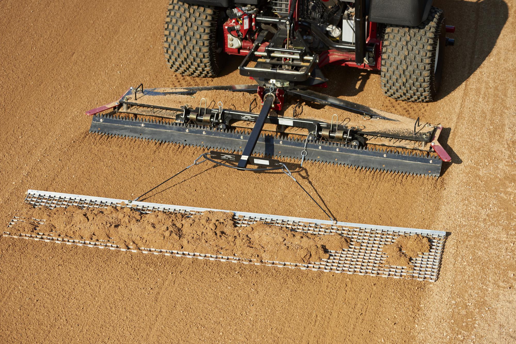 A red ride-on sand rake grooming a sandy surface with a wide metal rake attachment