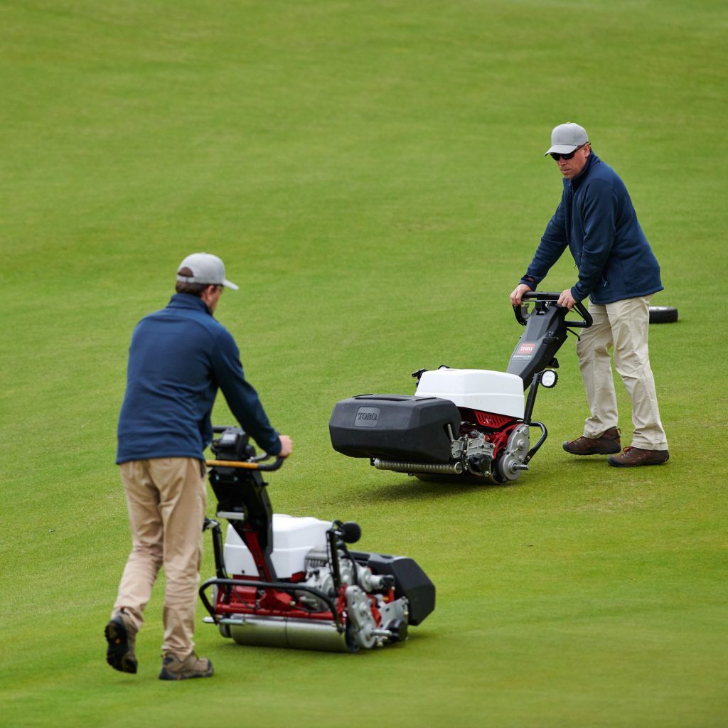 Two operators using Toro walk-behind mowers on a well-maintained golf green