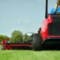 A person operates a red zero turn mower on a grassy field, showcasing its rear discharge feature