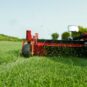 A red zero turn mower cutting grass with a large deck, showing grass clippings flying