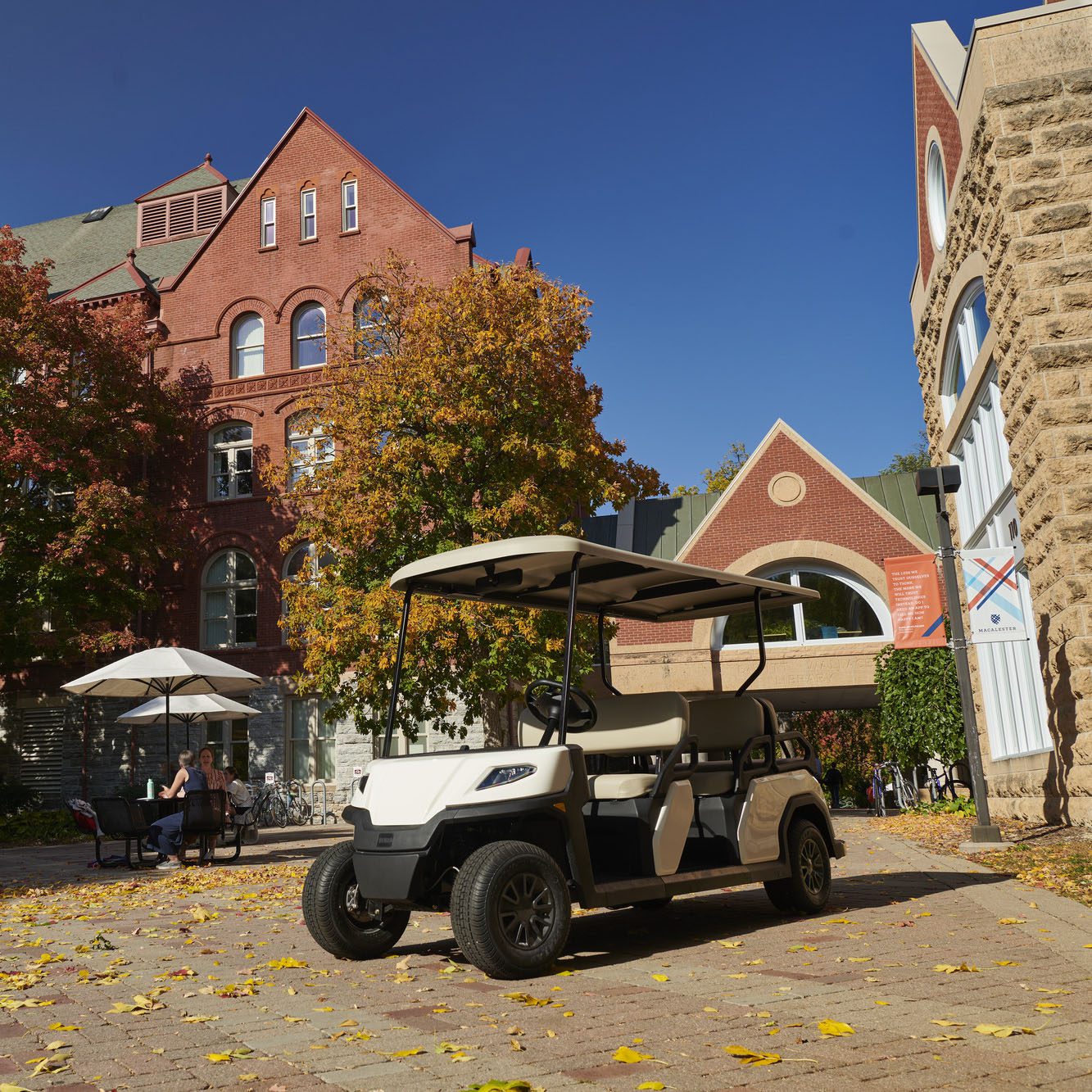 Toro Vista 6-seater golf cart parked in courtyard with red brick buildings and autumn trees Toro Vista 6-seater golf cart parked near red brick buildings, surrounded by autumn leaves and sunlight, offering spacious seating for passengers