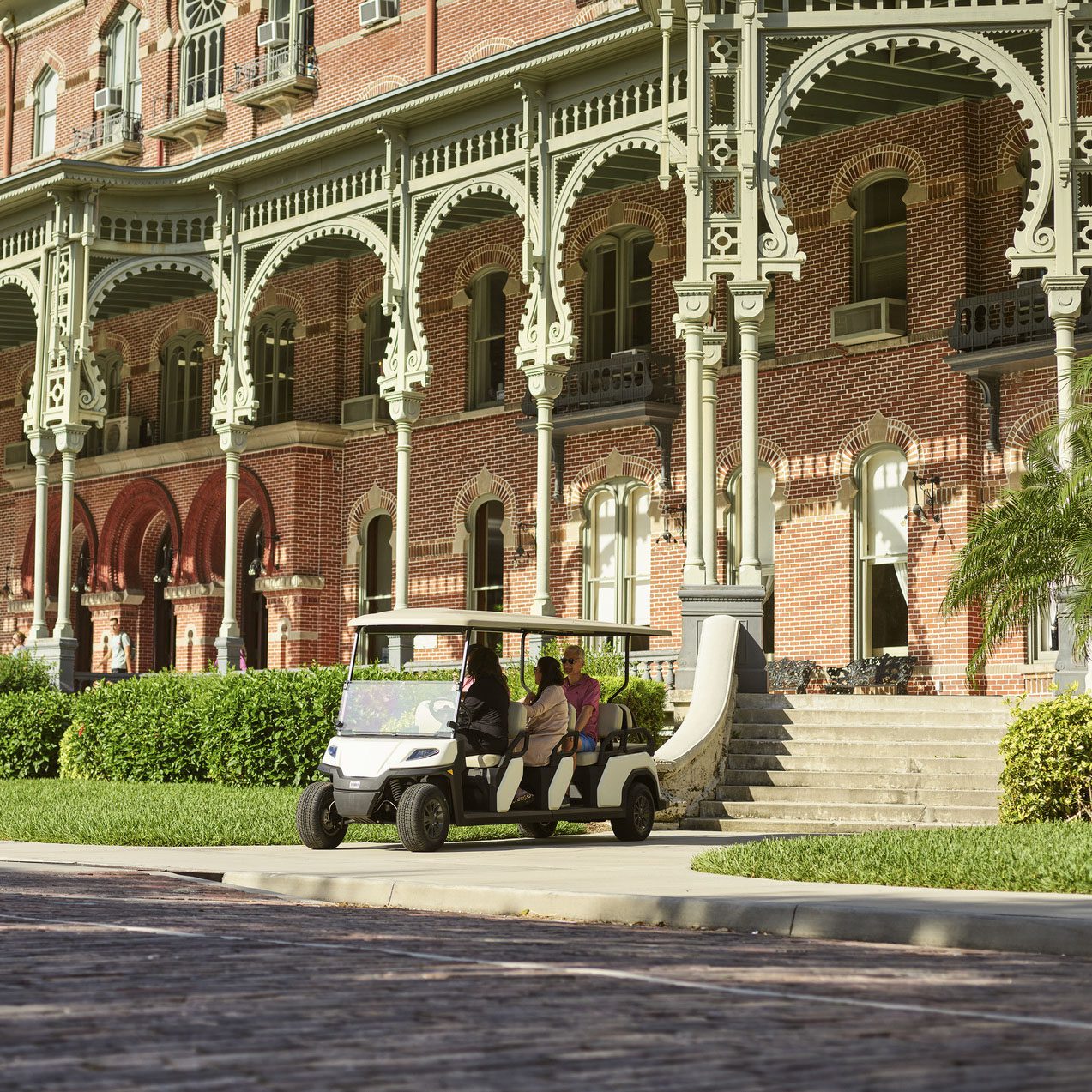 Toro Vista 8-seater golf cart driving by historic brick building with ornate columns Toro Vista 8-seater golf cart with beige seats and a white roof, transporting passengers past a historic brick building with intricate architectural details