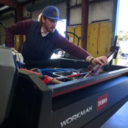 A worker inspects tools in the back of a Toro utility vehicle in a workshop setting