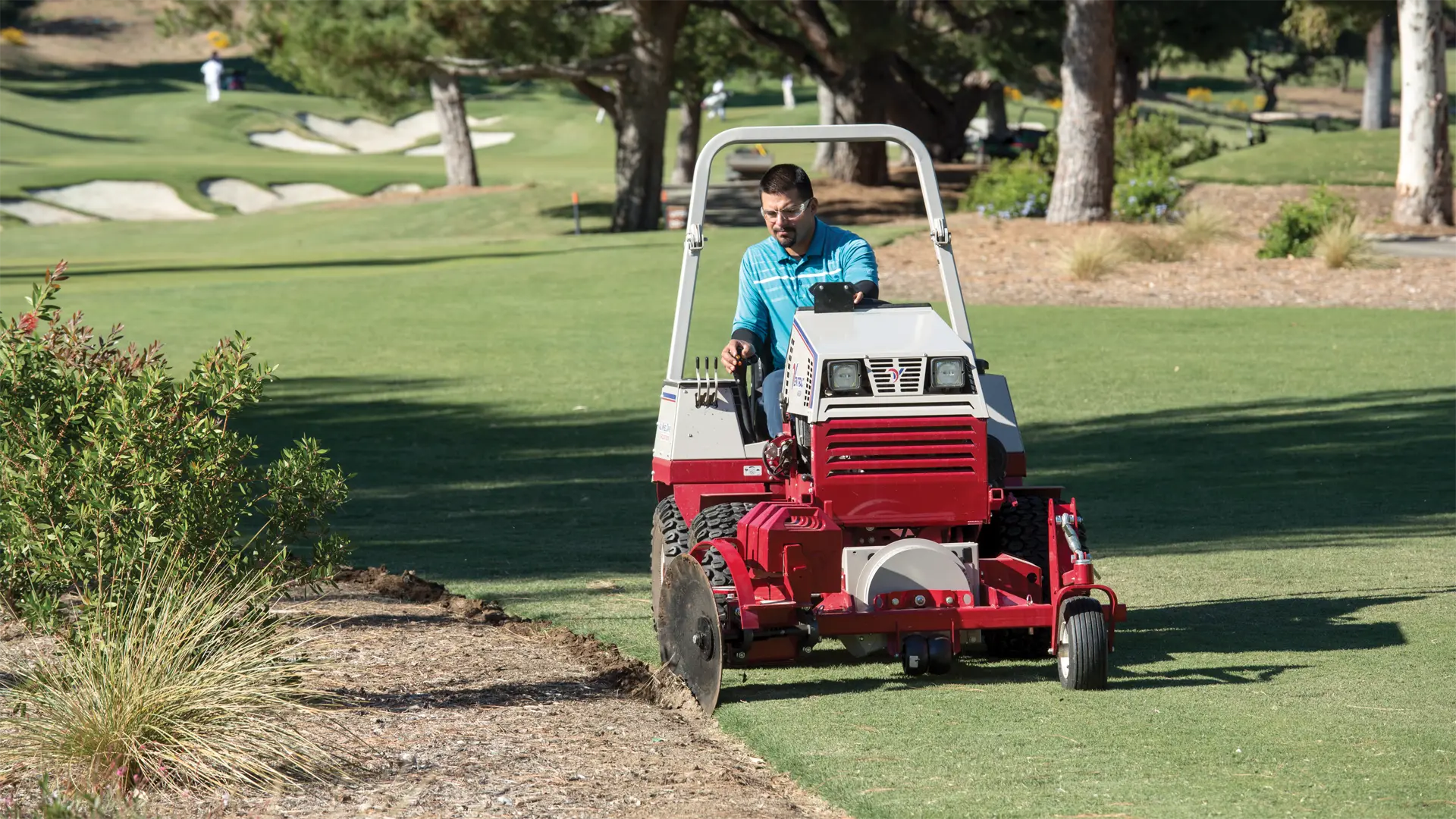 ED200_Annondale_5858-L1920 A man operates a red tractor attachment, edging a flower bed on a golf course