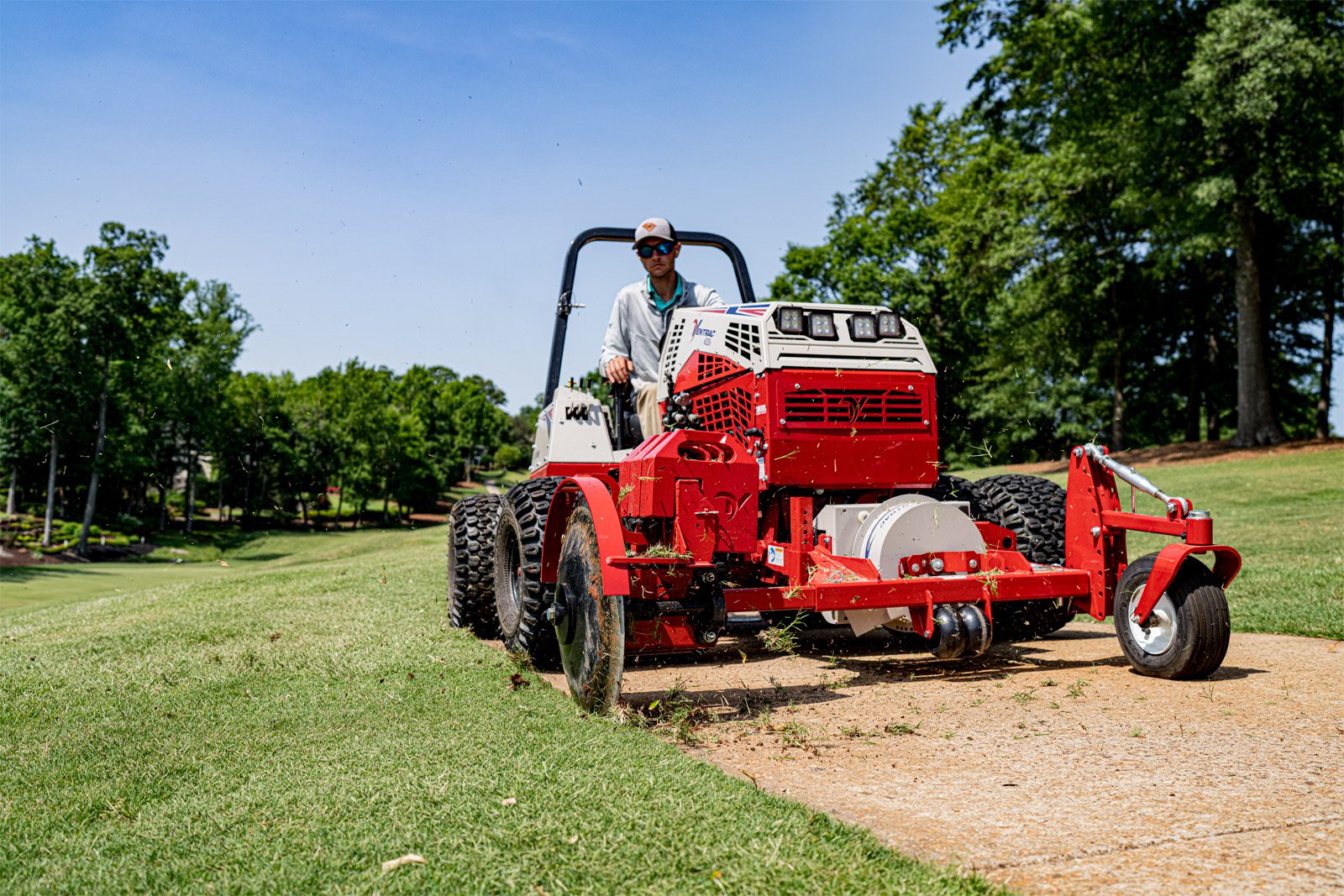 A red Ventrac machine operates on a golf course, maneuvering on grass near a fairway