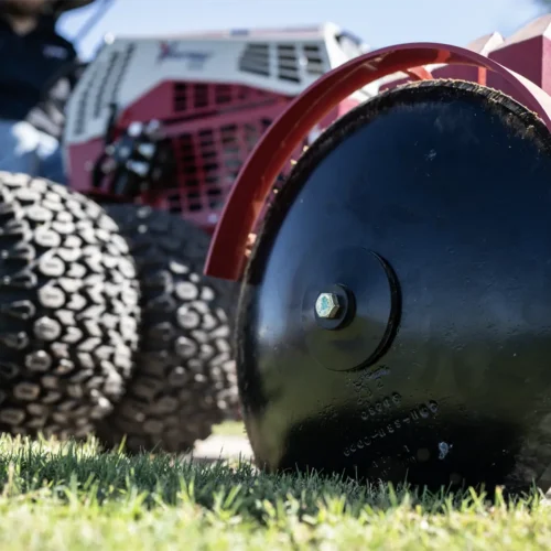 Close-up of a black edger wheel on grass, with a tractor attachment blurred in the background