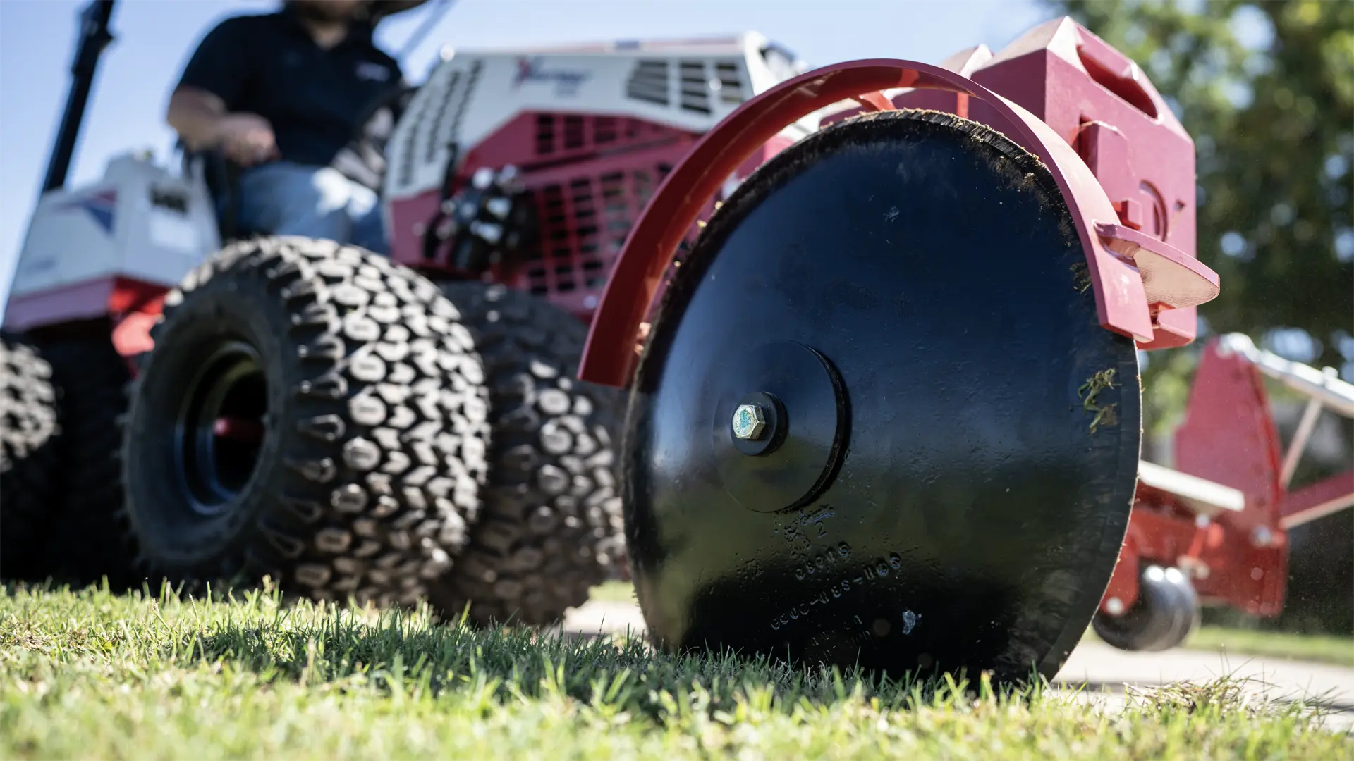 ED_Greg_Hall_Louisiana_06210-L1920 Close-up of a black edger wheel on grass, with a tractor attachment blurred in the background