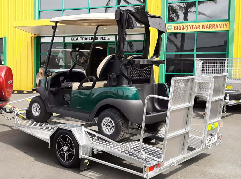Golf-Cart A green golf cart on a low-deck trailer with a light ramp and mag wheels outside a building