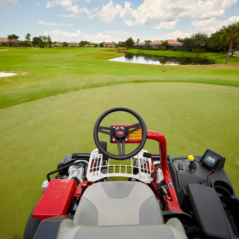 View from the seat of a Toro ride-on greens mower, showcasing the steering wheel and dashboard on a golf course