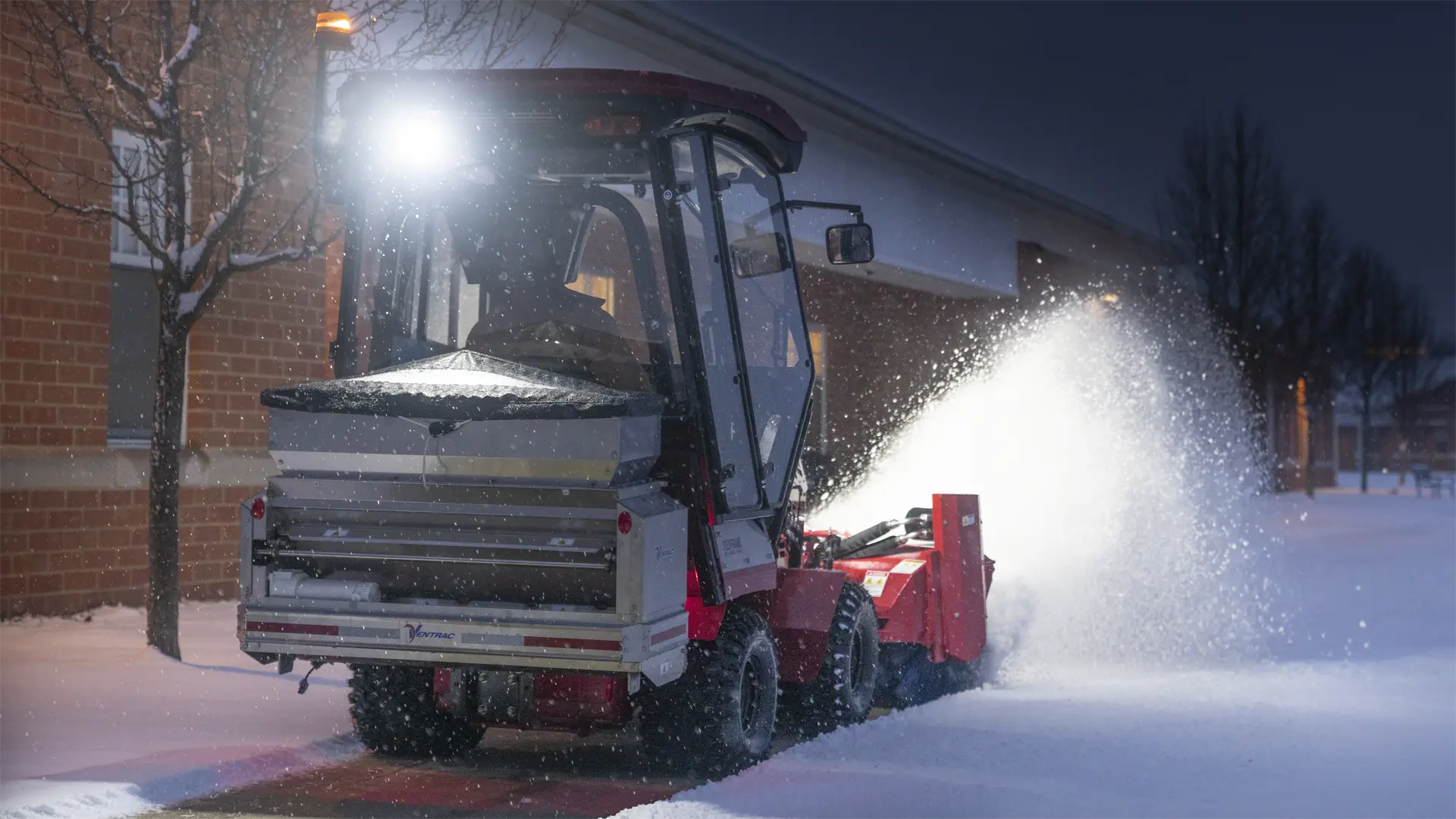 KJ520_4520_Orrville02_1-31-21_ (303)-L1920 A tractor attachment clears snow from a walkway, illuminated by a bright front light at night