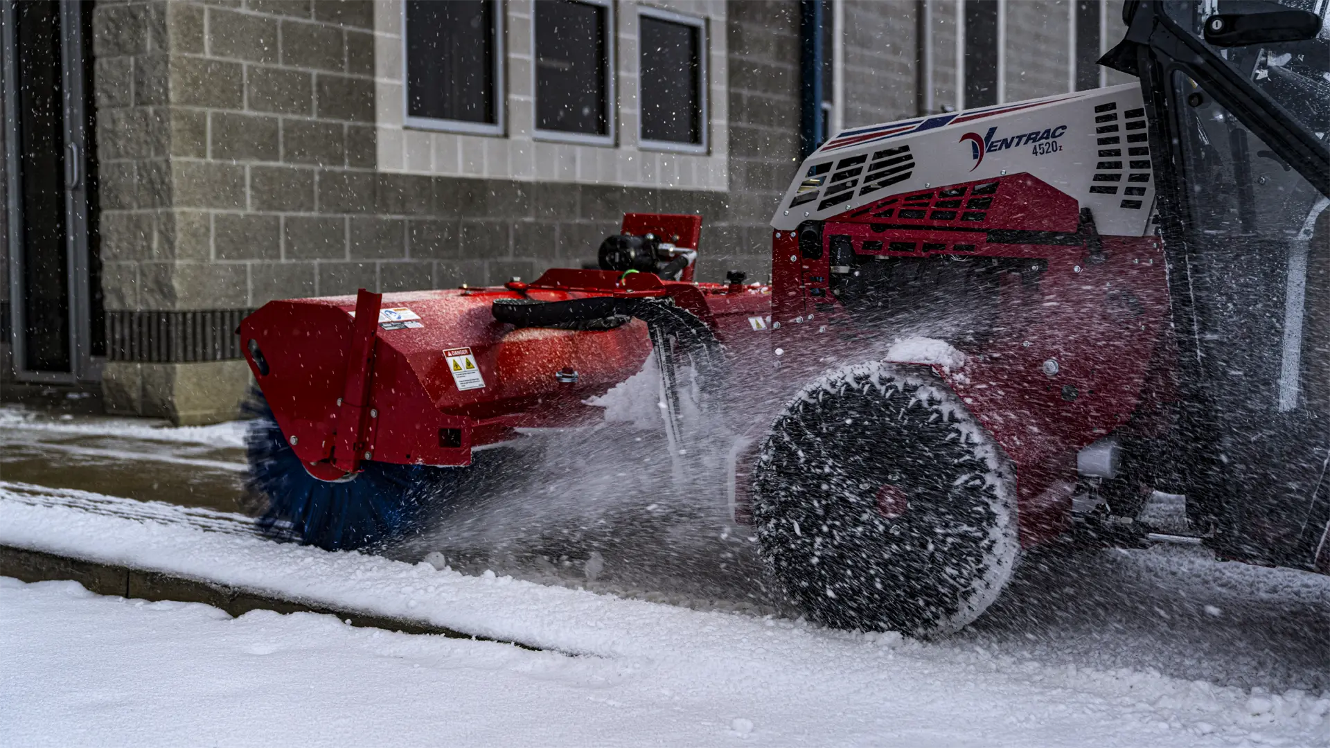 KJ520_4520_Orrville02_1-31-21_ (62)-L1920 A red tractor attachment sweeping snow from a walkway, showcasing its brush and operational design