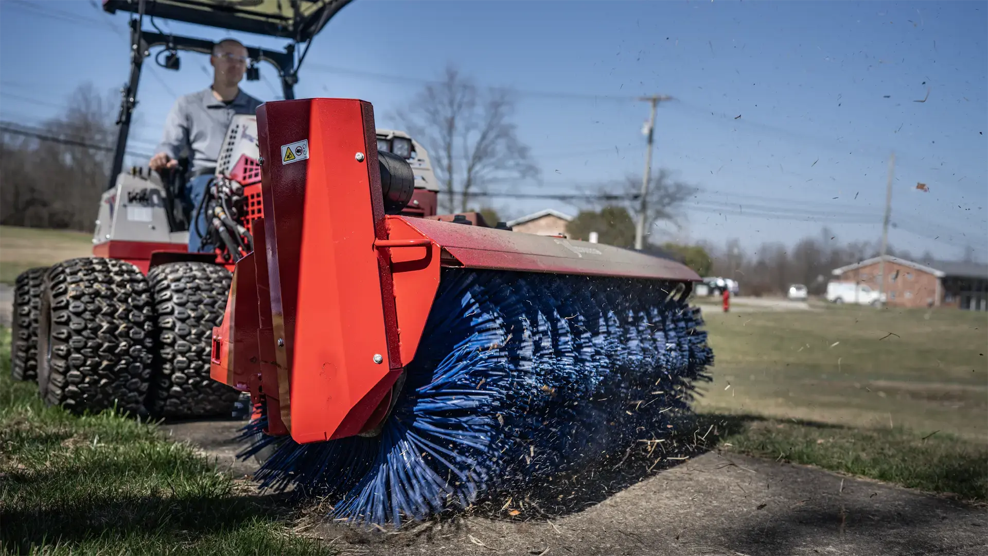 KJ_Broom_Orrville_School_4172-L1920 A red broom attachment on a tractor sweeps dirt and debris from a grassy area