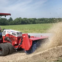 A red tractor attachment sweeps debris while a person operates it in a grassy outdoor setting