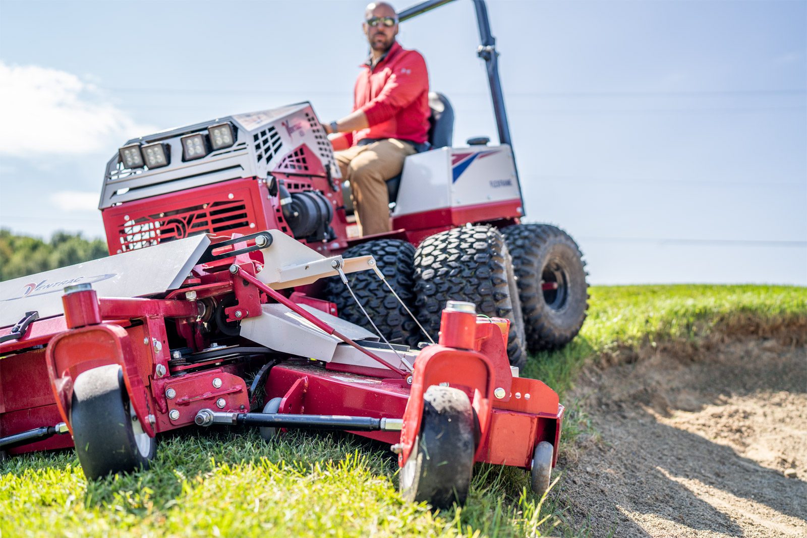 A Ventrac machine with a low profile chassis mows grass near a sand bunker on a golf course