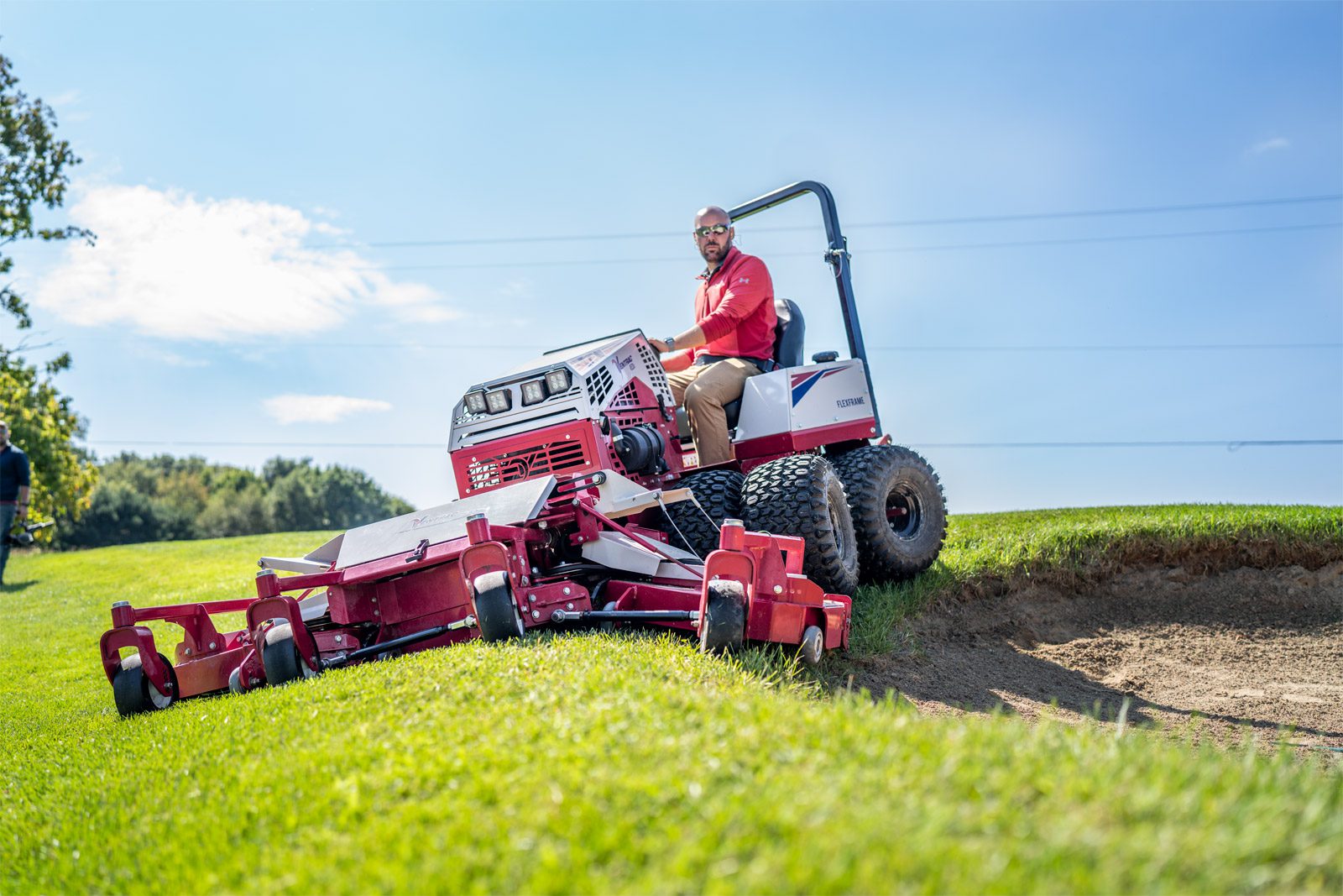 A Ventrac machine mows grass on a golf course slope under a clear blue sky