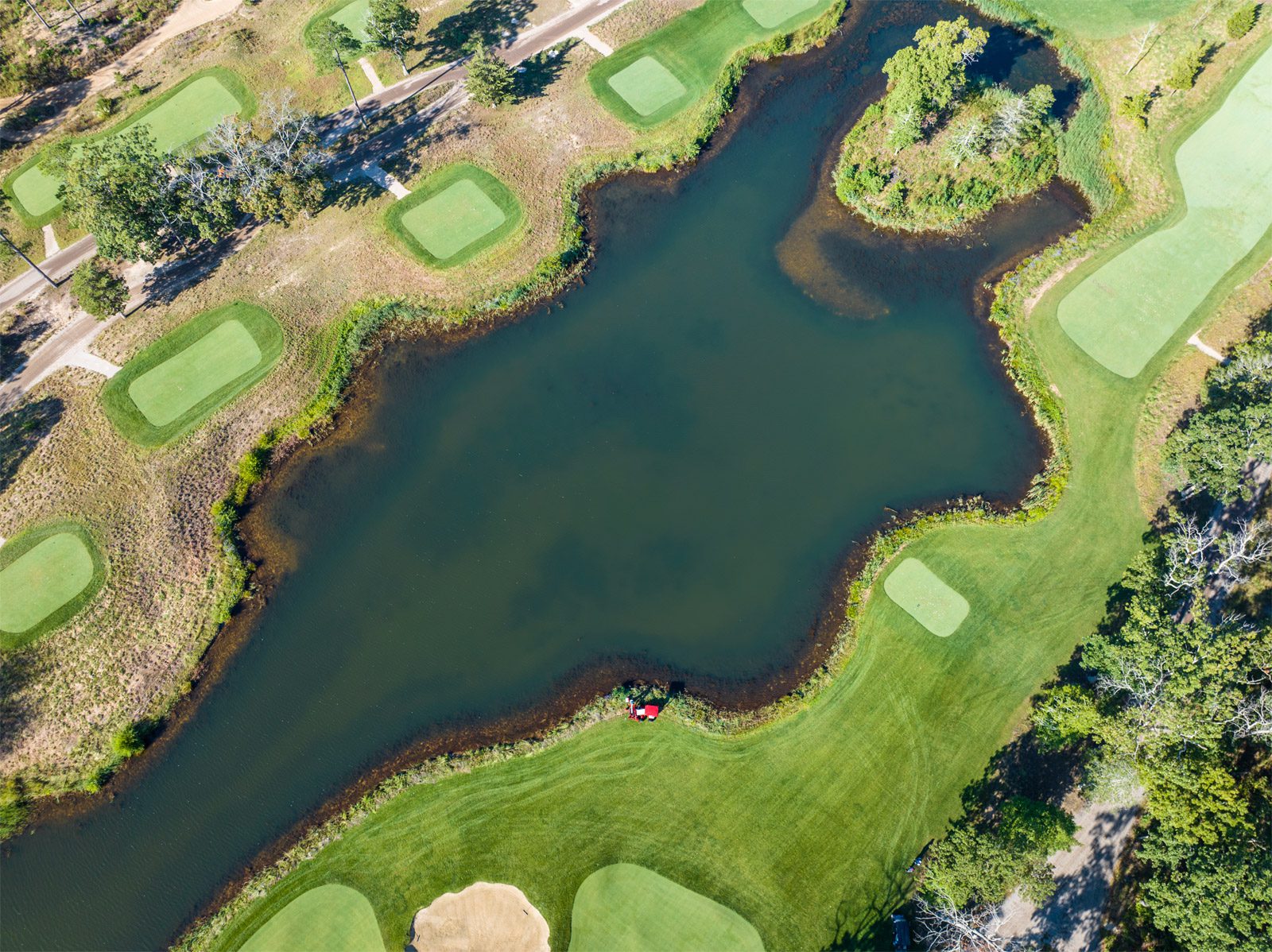 A red Ventrac machine near a pond, surrounded by golf course greens and fairways