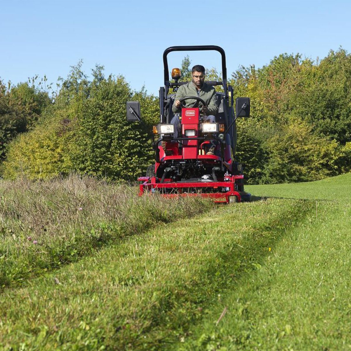 Pro Line H800 31051 Action 4 Red ride-on mower in action, cutting grass with a driver, surrounded by greenery and trees