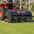 A Toro turf aerator attached to a tractor, featuring deep-tine heads and a hydraulic top link on grass