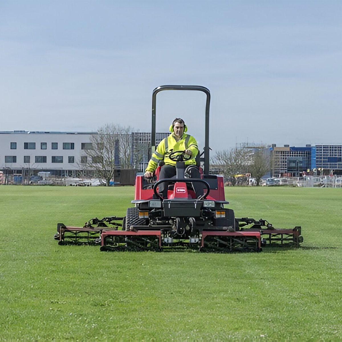 A heavy-duty mower in action on a grassy field, operated by a person wearing safety gear