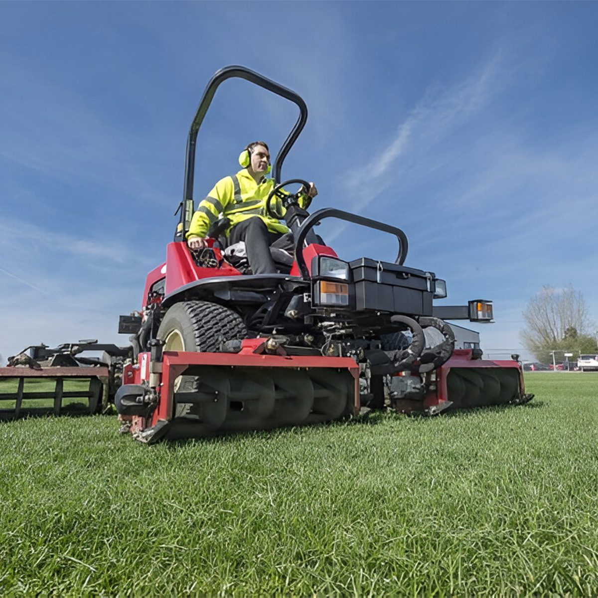A person operates a red mower on grass, showcasing its heavy-duty design and versatility in open spaces