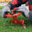 Red circular cutter tool being adjusted on artificial turf with gloved hands