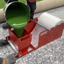 A red glue applicator with green adhesive being poured into the container for artificial turf installation
