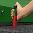 Hand holding a red and green measuring tool inserted into artificial turf surface for depth measurement