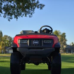 Red Toro utility vehicle facing forward on a grassy field with trees in the background