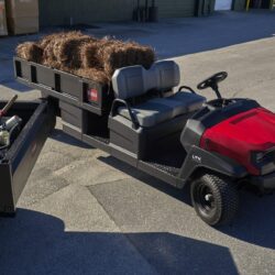 A red utility vehicle with a flatbed carrying hay bales, parked on a concrete surface