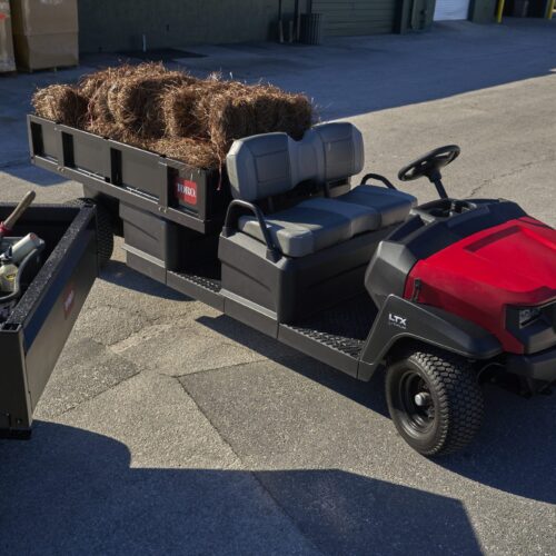 A red utility vehicle with a flatbed carrying hay bales, parked on a concrete surface