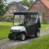A golf cart with a black weather enclosure parked on a gravel path near a house