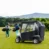 A golf cart with a weather shield parked on a green, two golfers walk in the background
