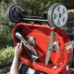 A person adjusts the blades of a red Toro lawn mower with gray wheels, showcasing its underside
