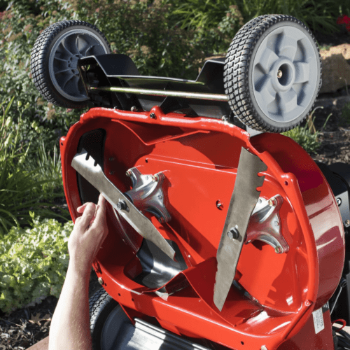 A person adjusts the blades of a red Toro lawn mower with gray wheels, showcasing its underside