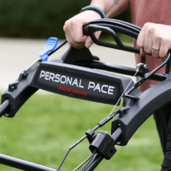 A person holds the handle of a Toro lawn mower, showcasing its Personal Pace feature in a green yard