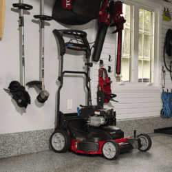 A Toro lawn mower is parked in a garage alongside gardening tools and equipment