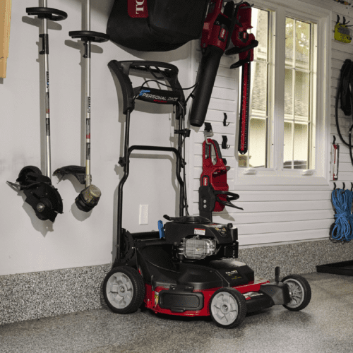 A Toro lawn mower is parked in a garage alongside gardening tools and equipment