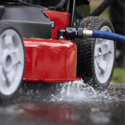 Close-up of a red lawn mower with a water hose attachment, showing water spraying from the deck