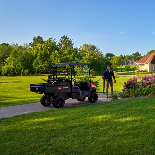 A black utility vehicle parked on a path, with a person walking nearby in a green landscape