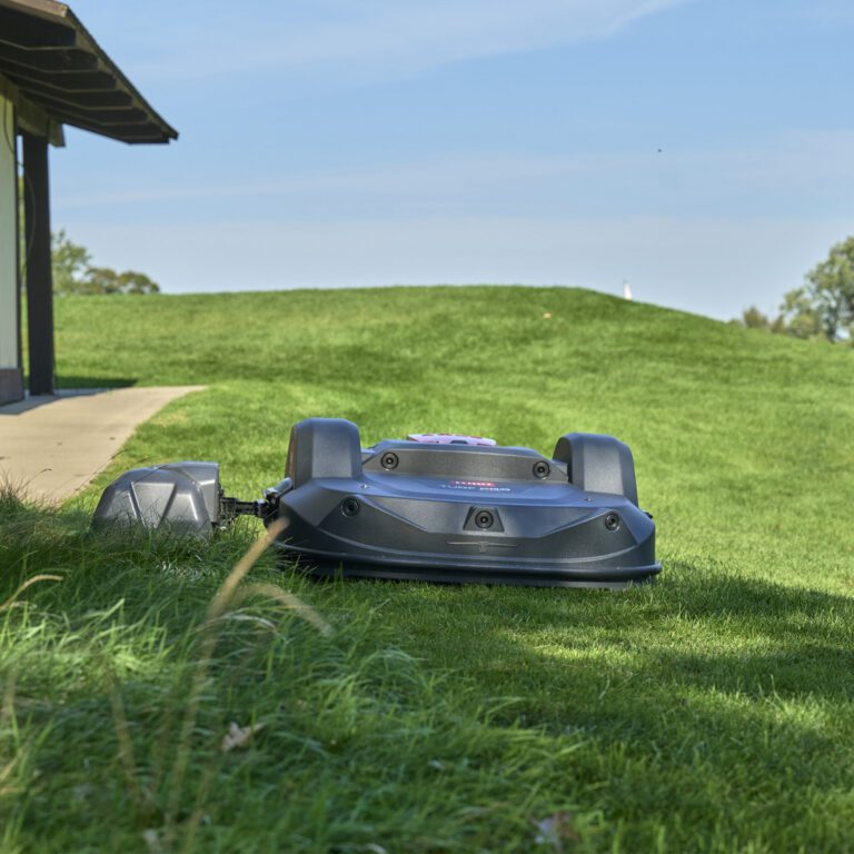 Autonomous mower positioned on a grassy slope, showcasing its sleek design and advanced cutting technology under a clear b…