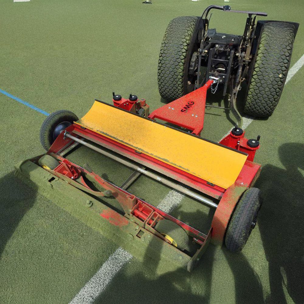SMG TurfCare TCA1400 artificial turf cleaner on synthetic field SMG TurfCare TCA1400 artificial turf cleaner attached to a vehicle, dragging behind to maintain synthetic sports turf.