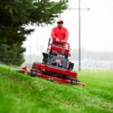 A person in a red shirt operates a Toro stand-on mower on a grassy slope