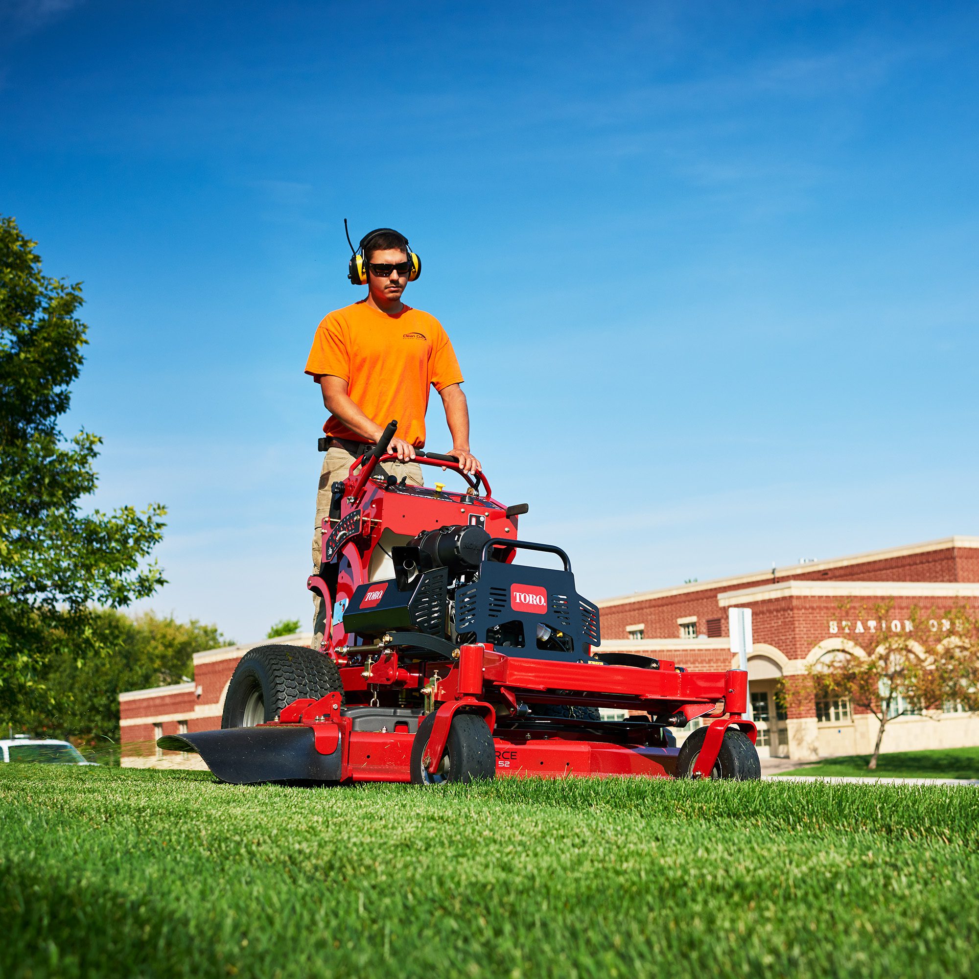 assetstorage-16 A person operates a red Toro stand-on mower on a grassy area under a clear blue sky
